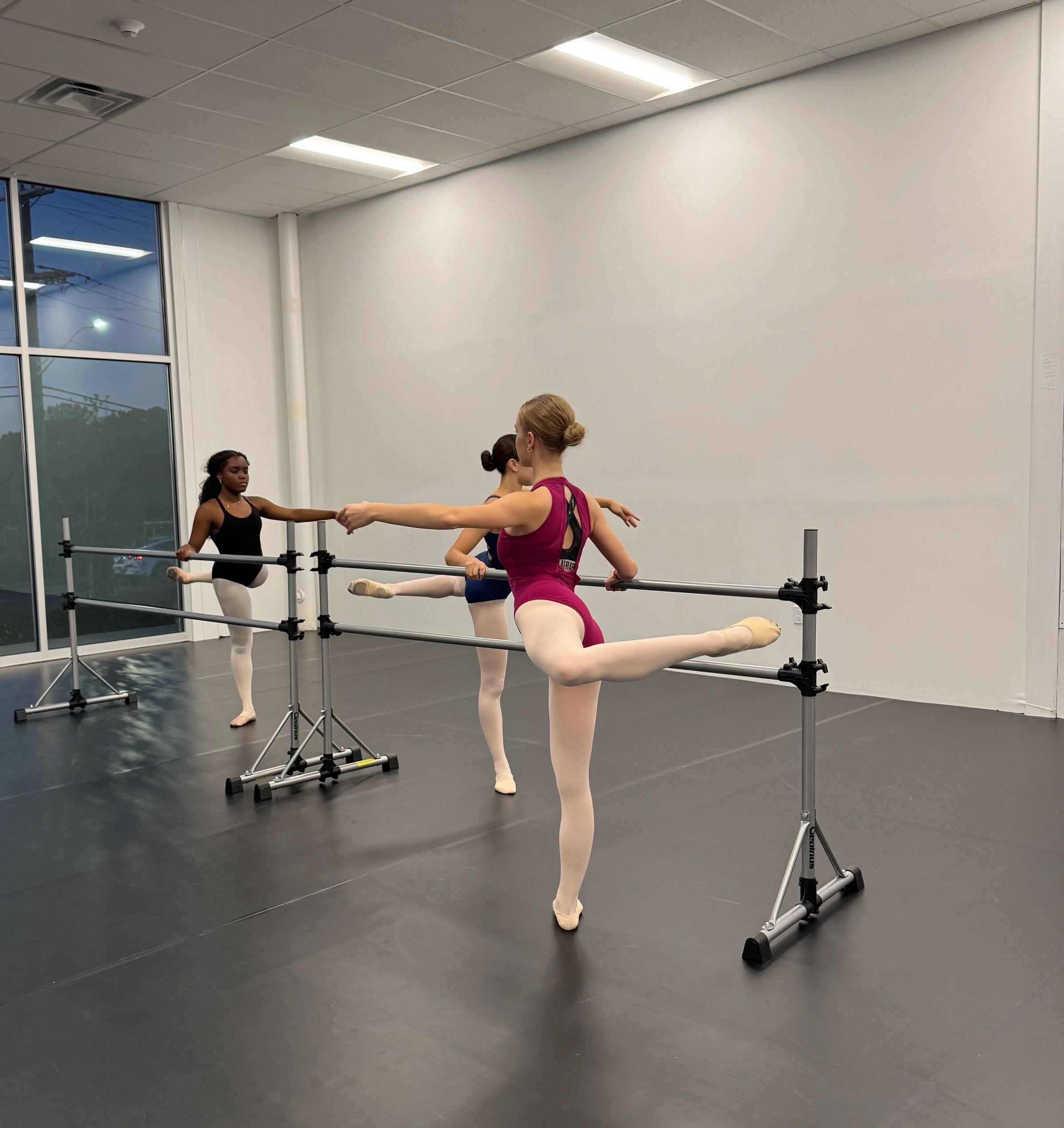 Three teen students at the ballet barre executing developpé in the Dance Athletics Studio.