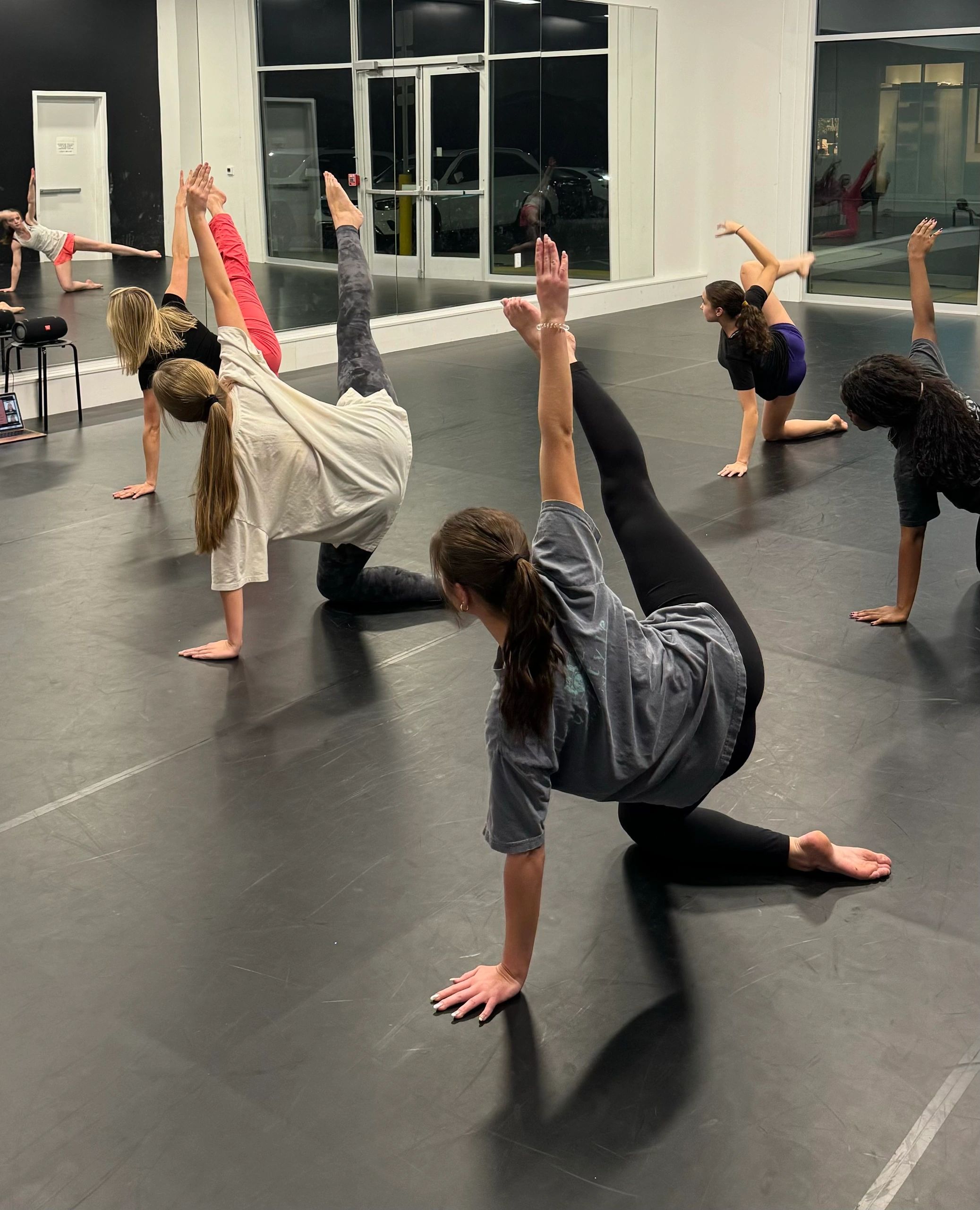 Teen dancers in a floor-work warm-up across the main studio.